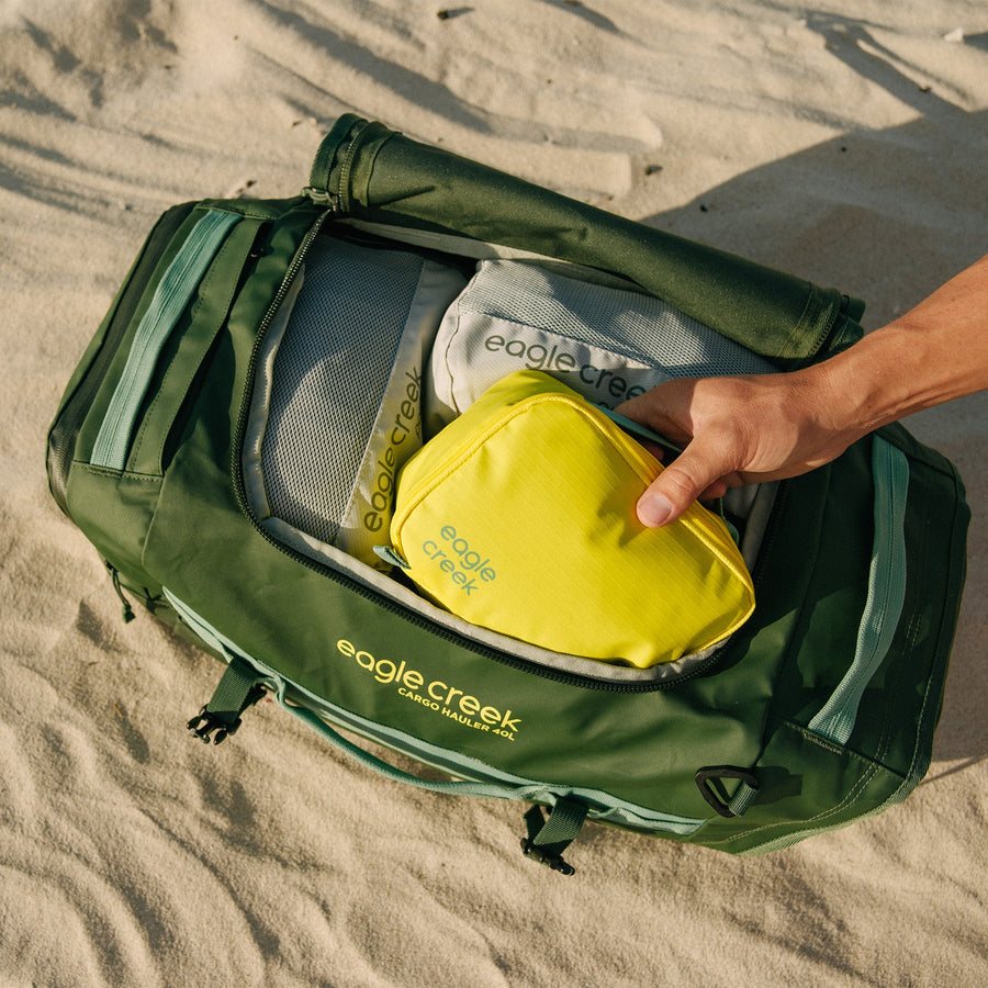 A green duffle bag filled with packing cubes on sand