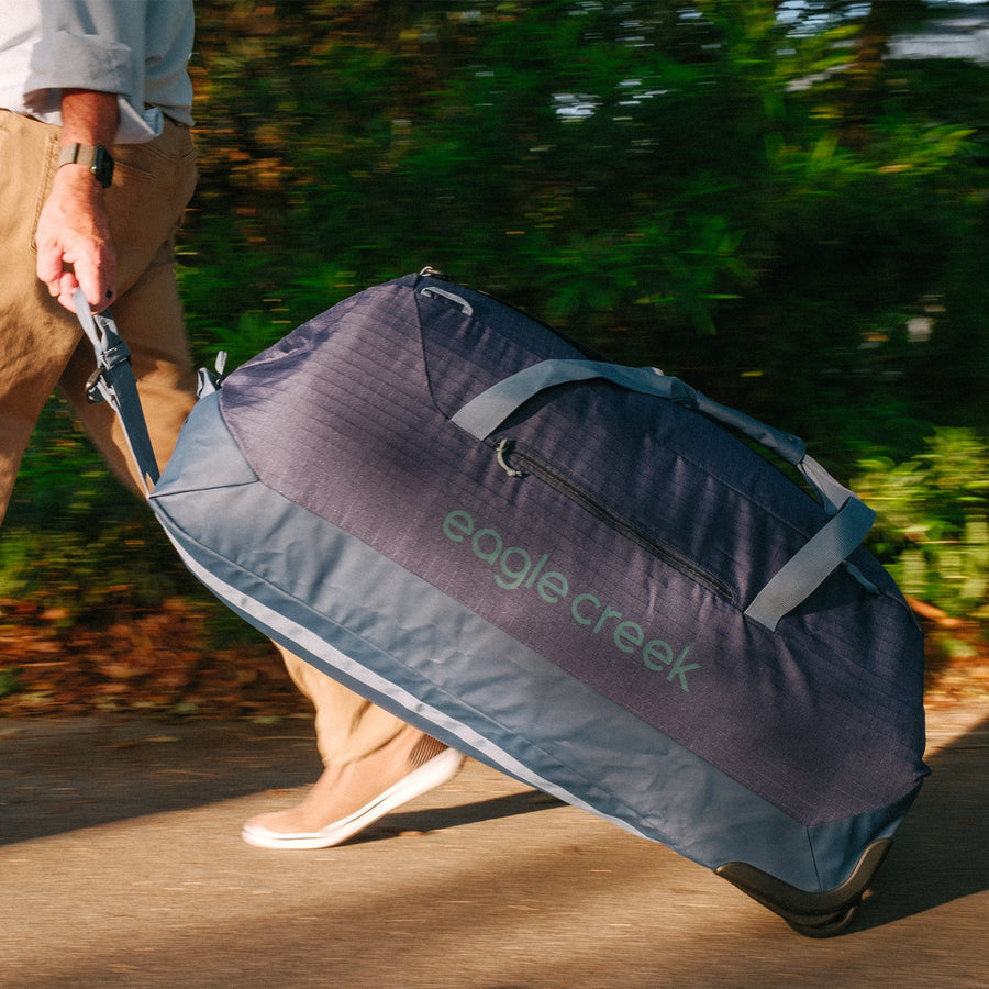 A person rolling a large navy blue duffle bag with wheels