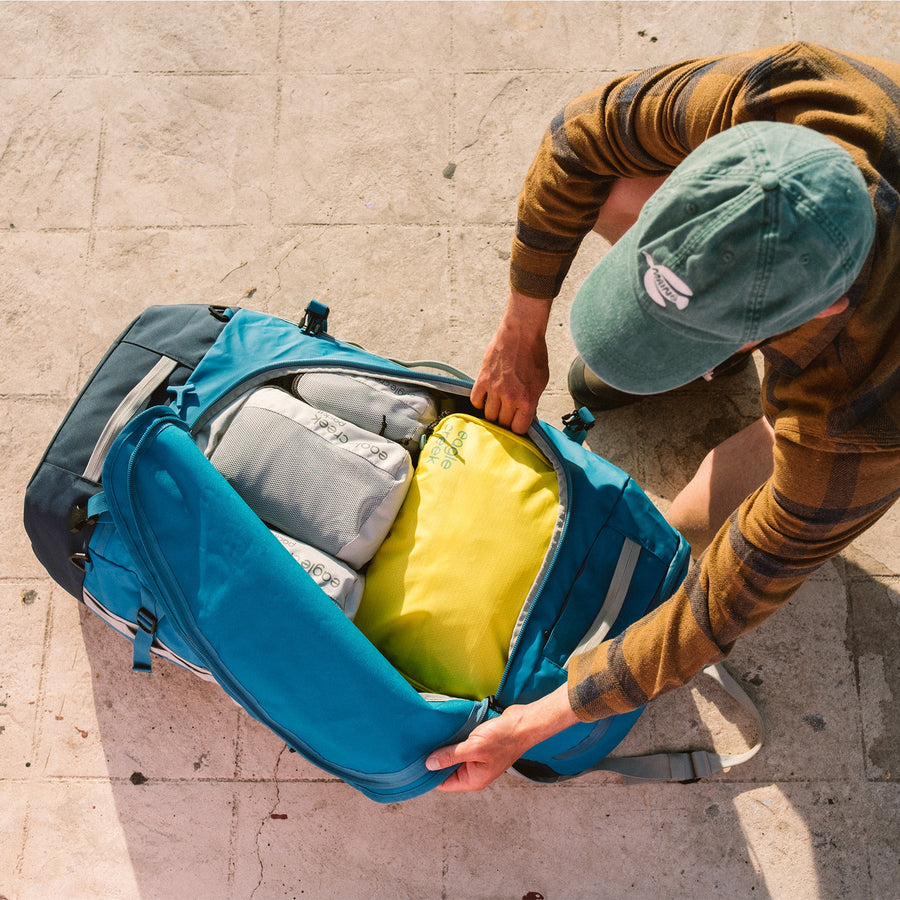A man opening a large blue duffle bag full of gray and yellow packing cubes