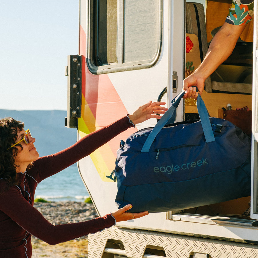 A person in a camper passes a navy blue duffle bag to outstretched arms