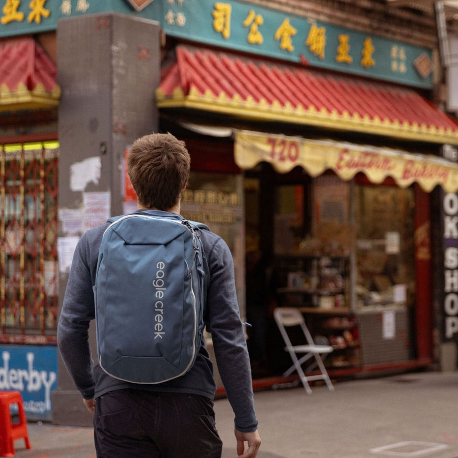 A person wearing a blue travel backpack outside of a shop.